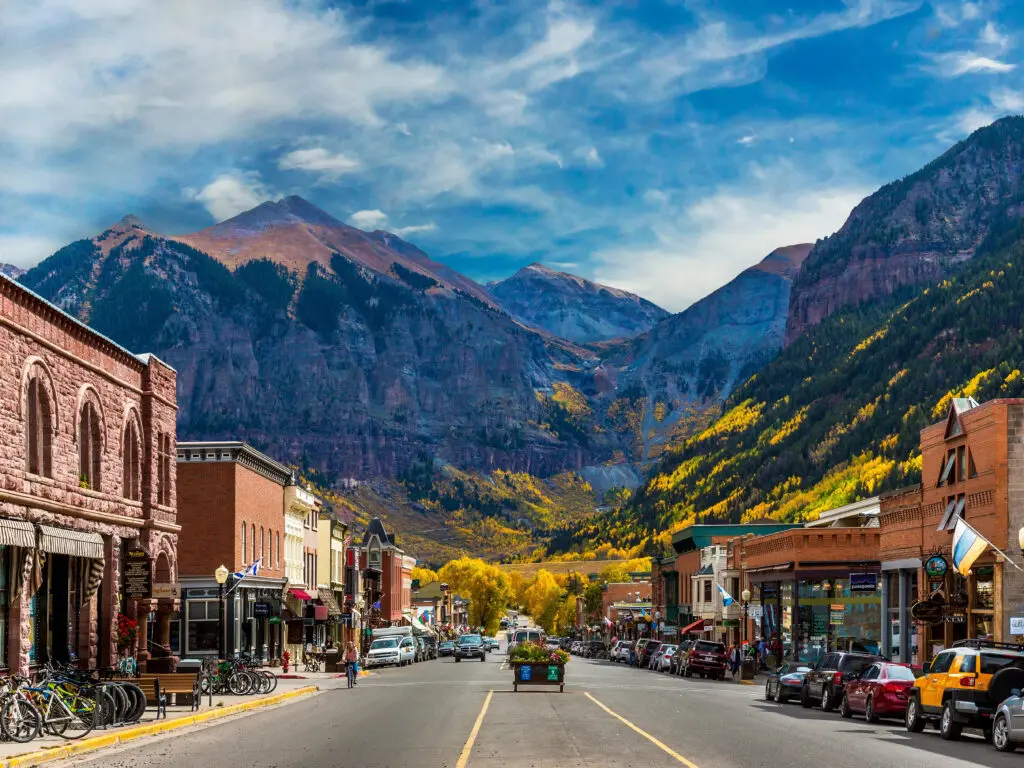 Historic downtown Telluride main street with Victorian brick buildings, autumn golden aspen trees on mountainsides and dramatic San Juan peaks