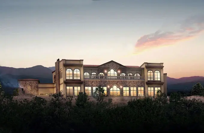 Contemporary Tuscan-style estate at twilight with two-story stone architecture, arched windows, illuminated interior and mountain silhouettes at dusk