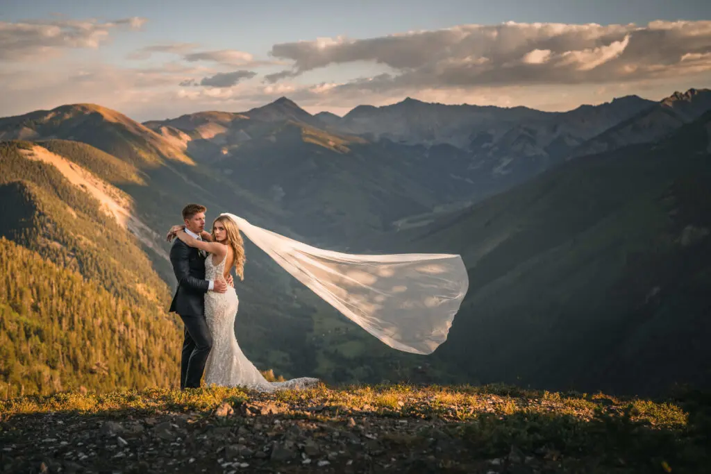 Groom and bride atop Aspen Mountain as her veil blows in the wind