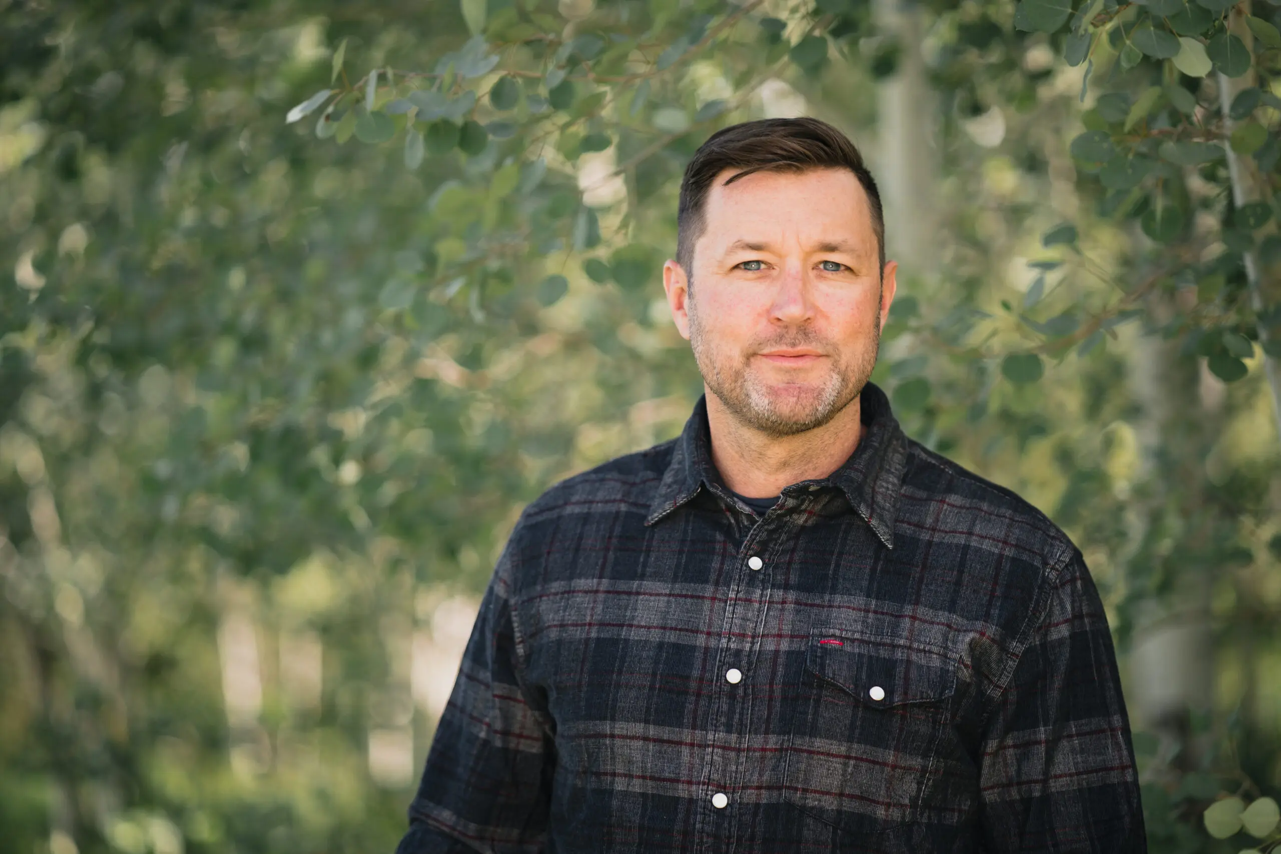 Professional environmental headshot framed by green foliage.