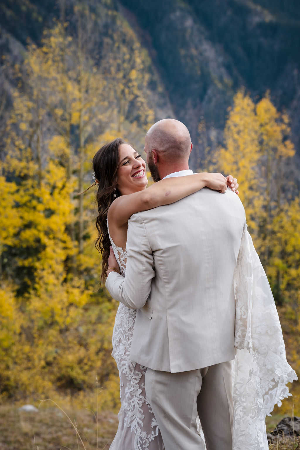 A joyful close-up of the bride laughing while wrapped in the groom’s arms. The background is filled with the soft, out-of-focus yellow of autumn aspen trees.