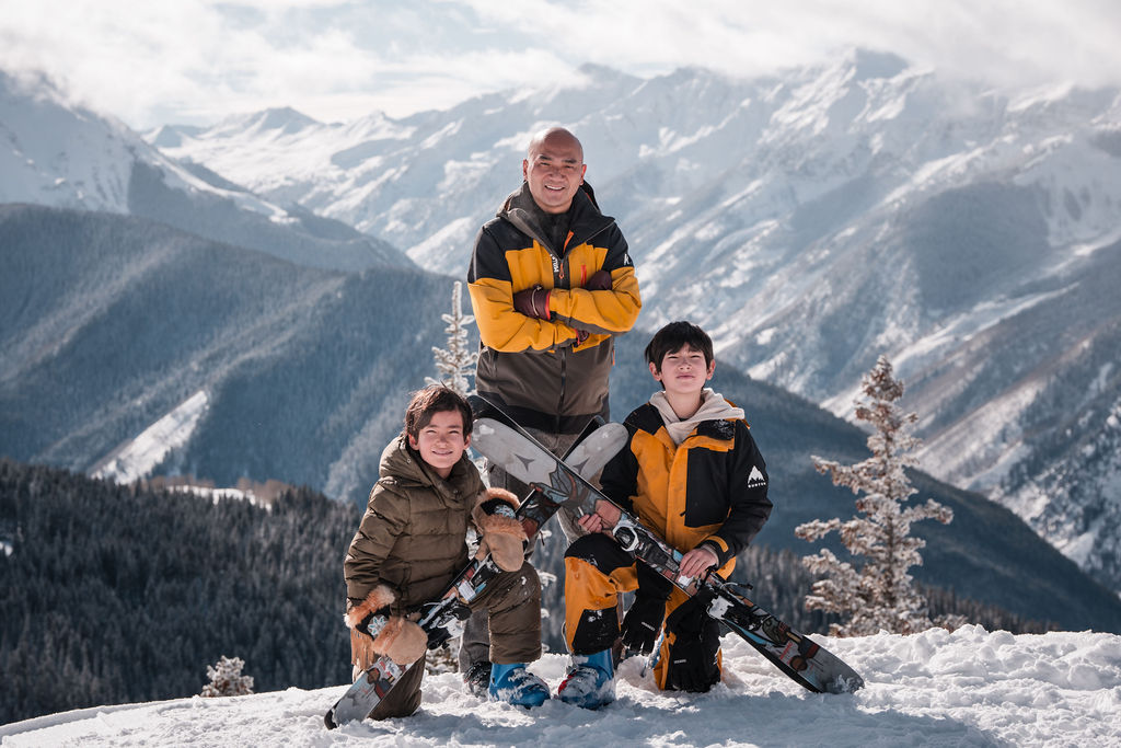A family in vibrant winter gear posing on a mountain ridge, captured by a professional Aspen Family Ski Videographer to document their vacation adventures.