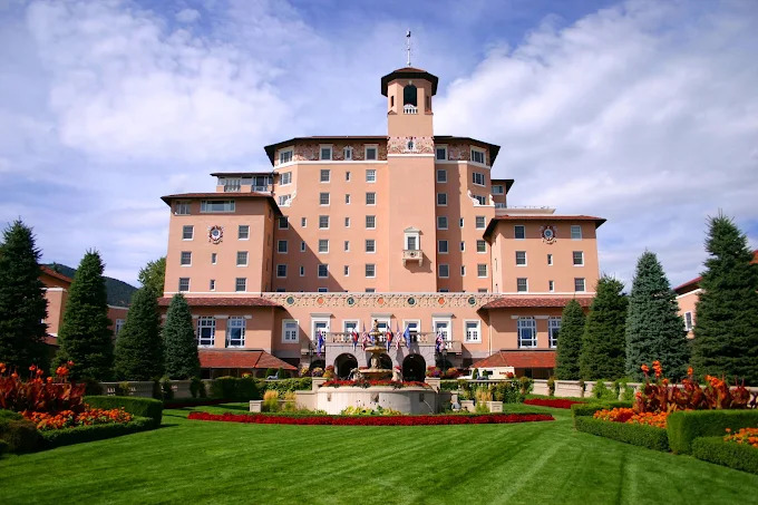 The Broadmoor resort, iconic pink Mediterranean-style luxury hotel with central tower, manicured lawn fountain, vibrant flower gardens and mountain backdrop - elegant wedding venues in Colorado Springs