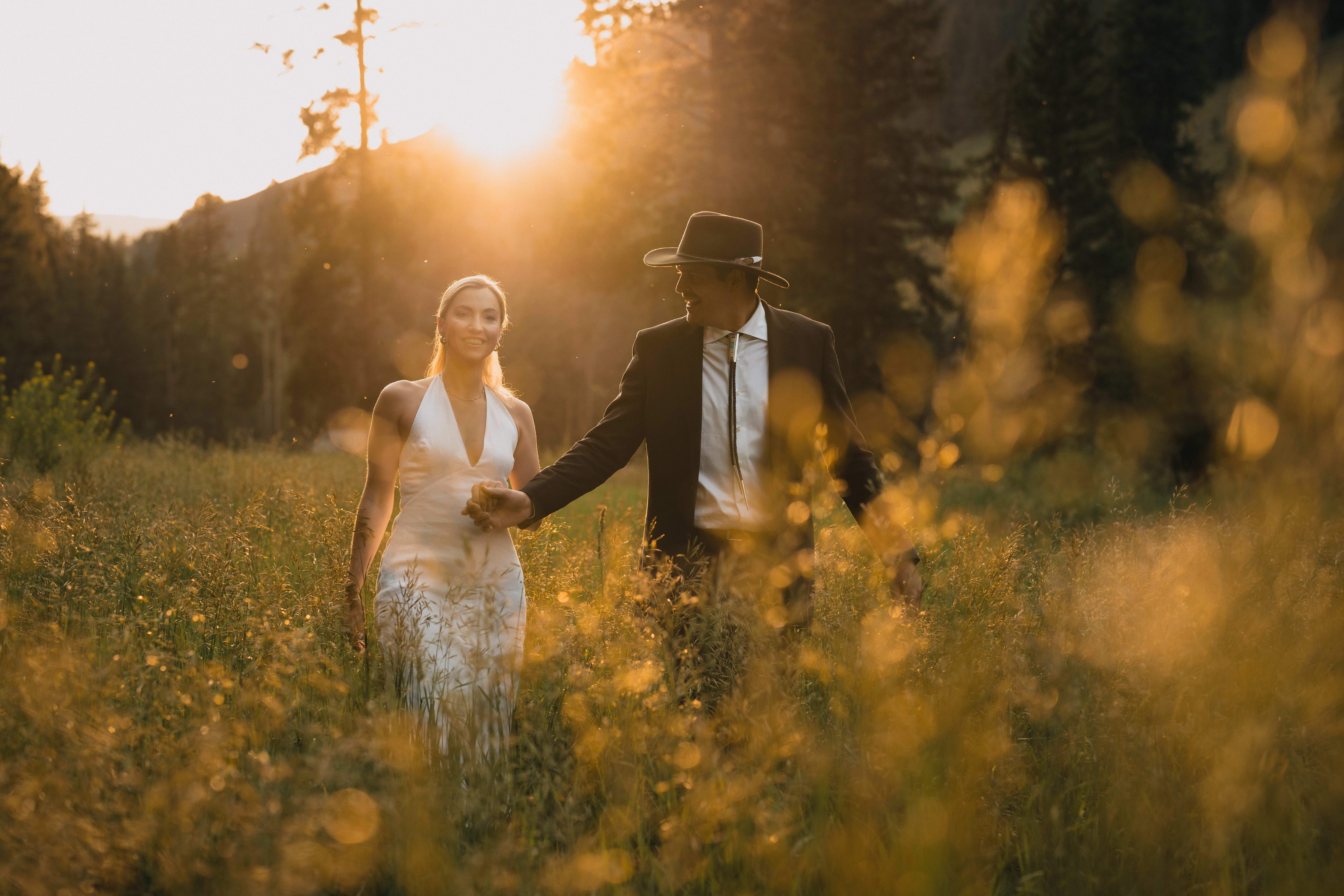 Bride and groom walk through the high grass at sunset in Colorado.
