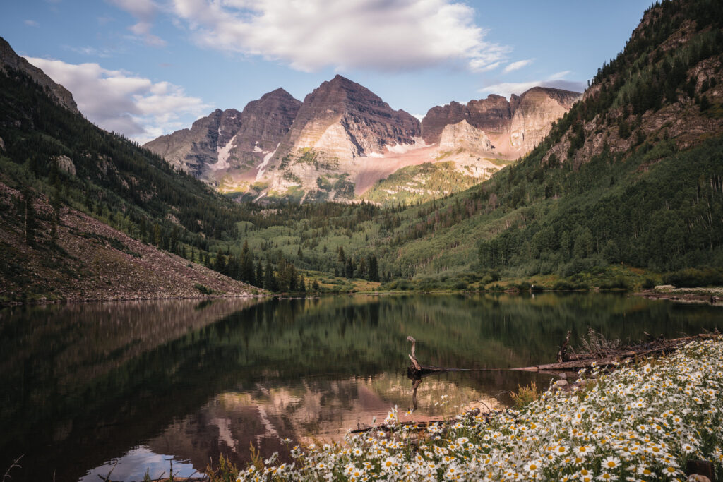 Scenic view of the Maroon Bells peaks reflected in the calm waters of Maroon Lake with surrounding evergreen trees and mountain landscape