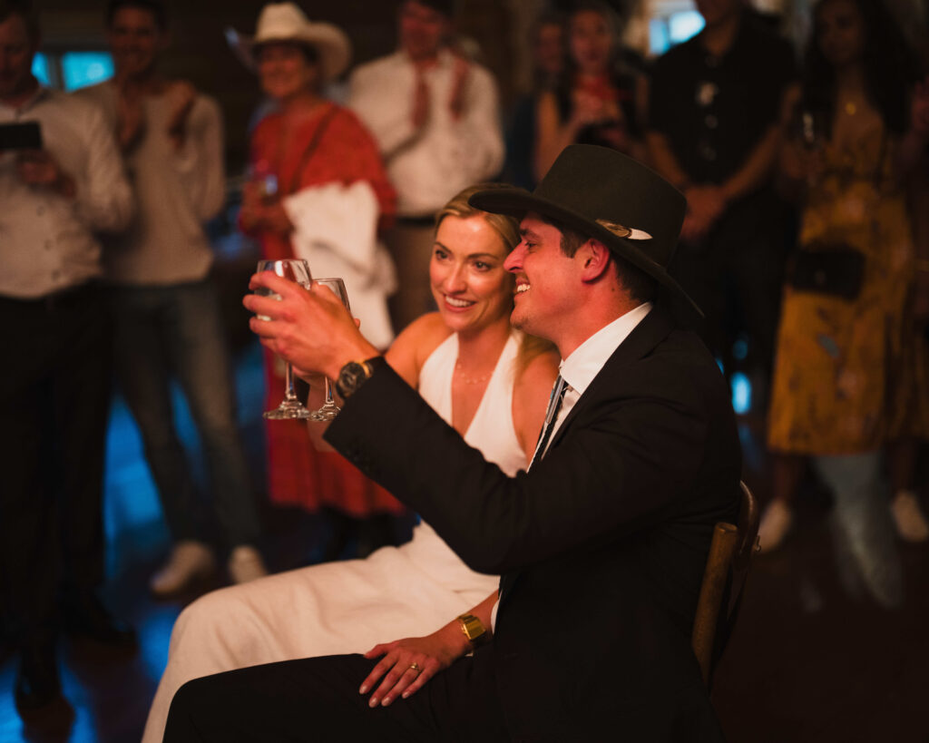 Bride and groom raising champagne glasses in toast with wedding guests celebrating in background