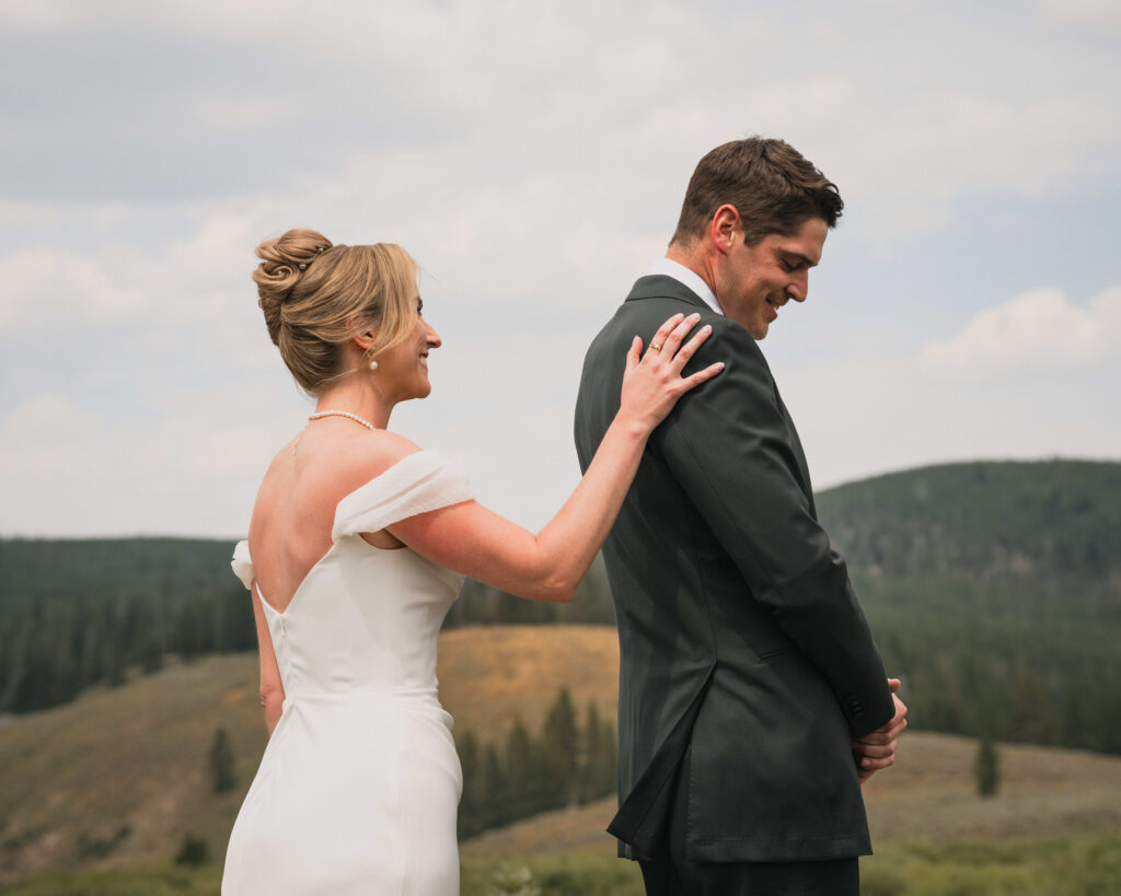 Bride touching the groom’s shoulder during a first-look moment on a mountain overlook in Colorado.