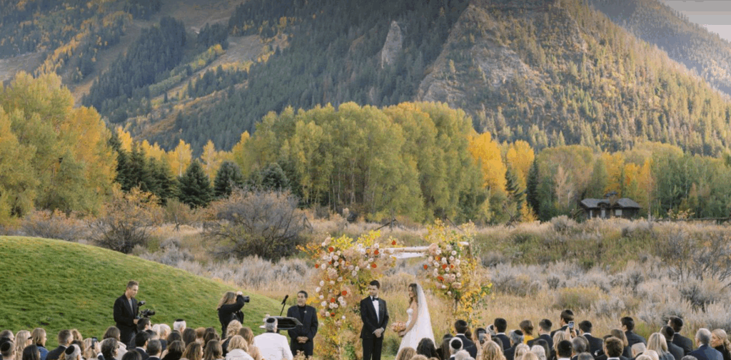 A bride and groom exchange vows outdoors at Aspen Meadows, surrounded by mountain views and open meadows.