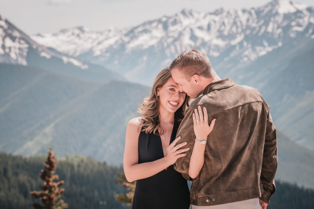 Couple photographed during an engagement session on a Vail Colorado mountain overlook with snowy peaks in the background, captured by Summit Photo and Film wedding photographers.
