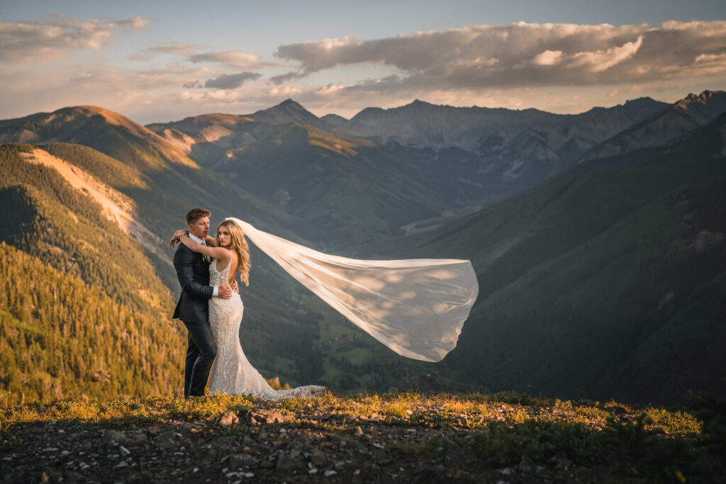 A groom and his new bride atop of the Aspen Mountains in Colorado as her veil blows delicately in the wind.