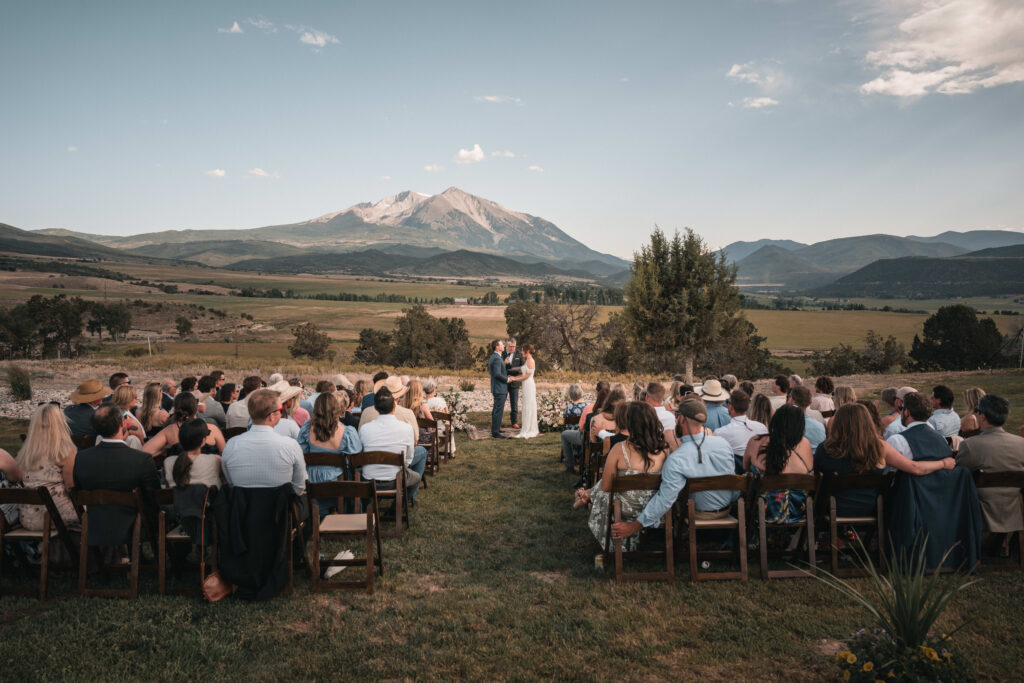 The bride and groom stand together during their wedding ceremony, framed by the towering Aspen mountains and scenic alpine landscape.