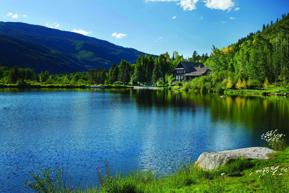 Scenic view of Dunbar Ranch in Aspen, Colorado, featuring a serene lake surrounded by lush green trees and mountains in the background.