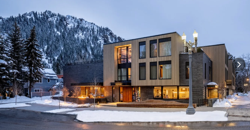 Exterior view of MOLLIE Aspen Hotel in downtown Aspen, Colorado, with modern architecture and mountain peaks in the background.