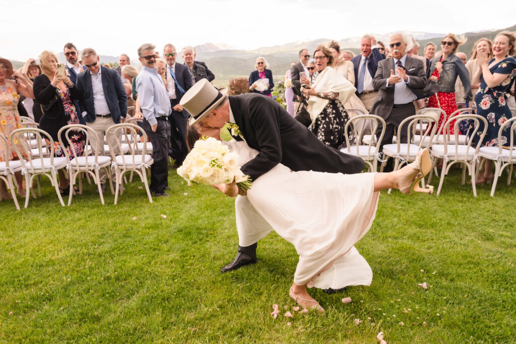 The groom playfully dipping the bride for a kiss on the ceremony lawn while guests cheer in the background at a Chaparral Ranch Wedding.
