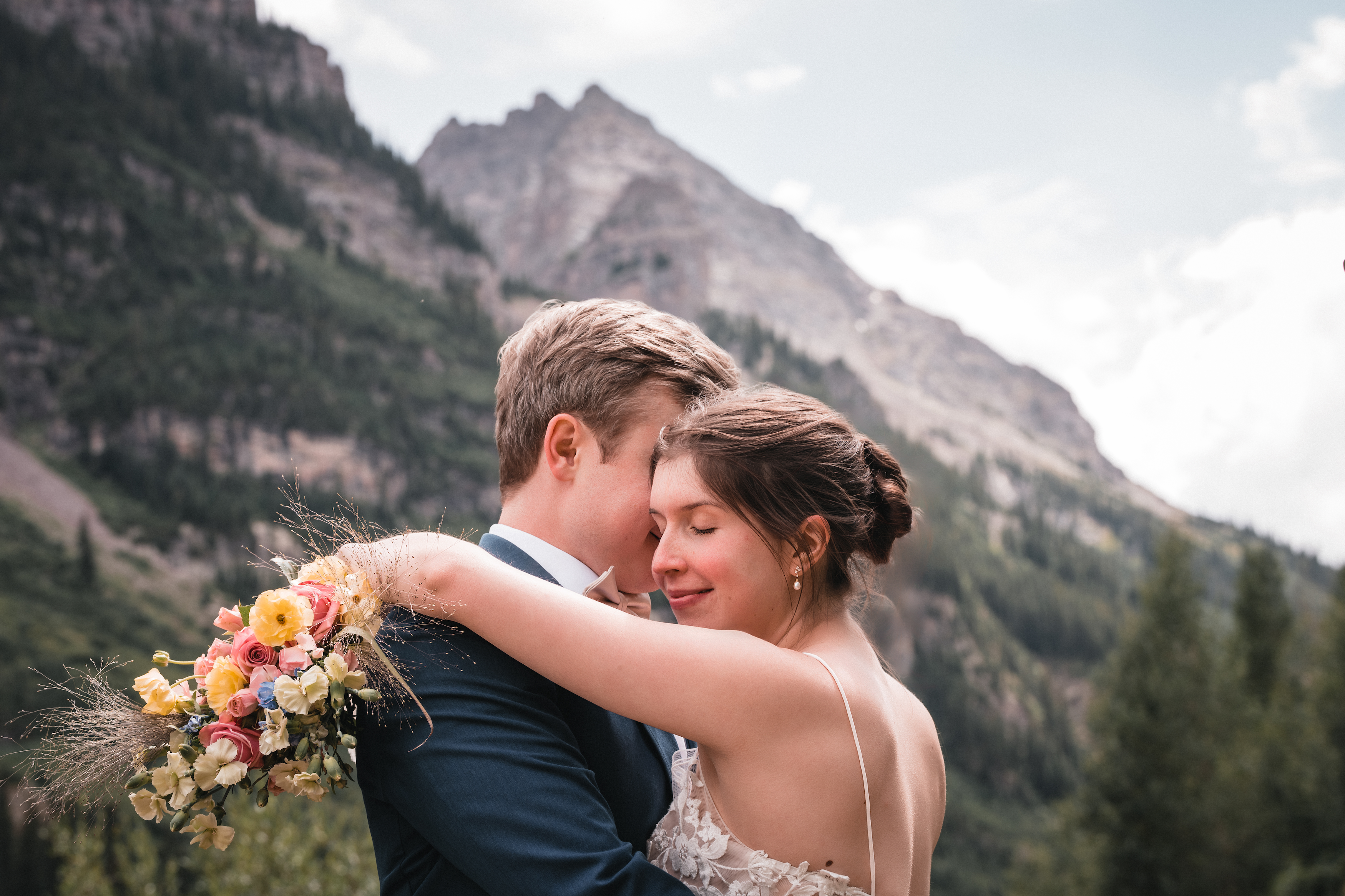 Groom kissing his bride at Maroon Bells, with the mountains rising behind them as she closes her eyes and holds him in a warm embrace.