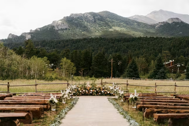 Outdoor ceremony setup at Wild Basin Lodge in Allenspark Colorado with log benches, floral aisle decor, and mountain views near Rocky Mountain National Park.
