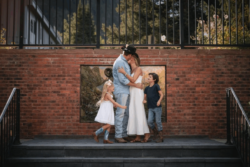 Husband and wife smiling at each other in their cowboy hats as their kids run around them on top of a staircase outside in Aspen.