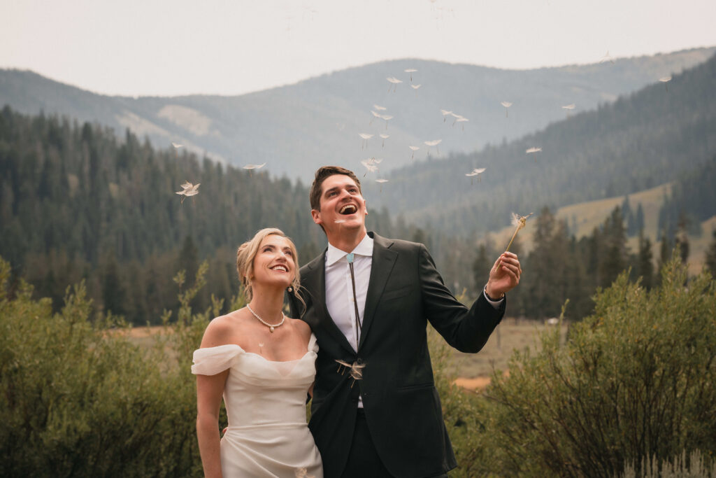 Bride and groom standing together at Maroon Bells, watching flower petals float through the air around them.