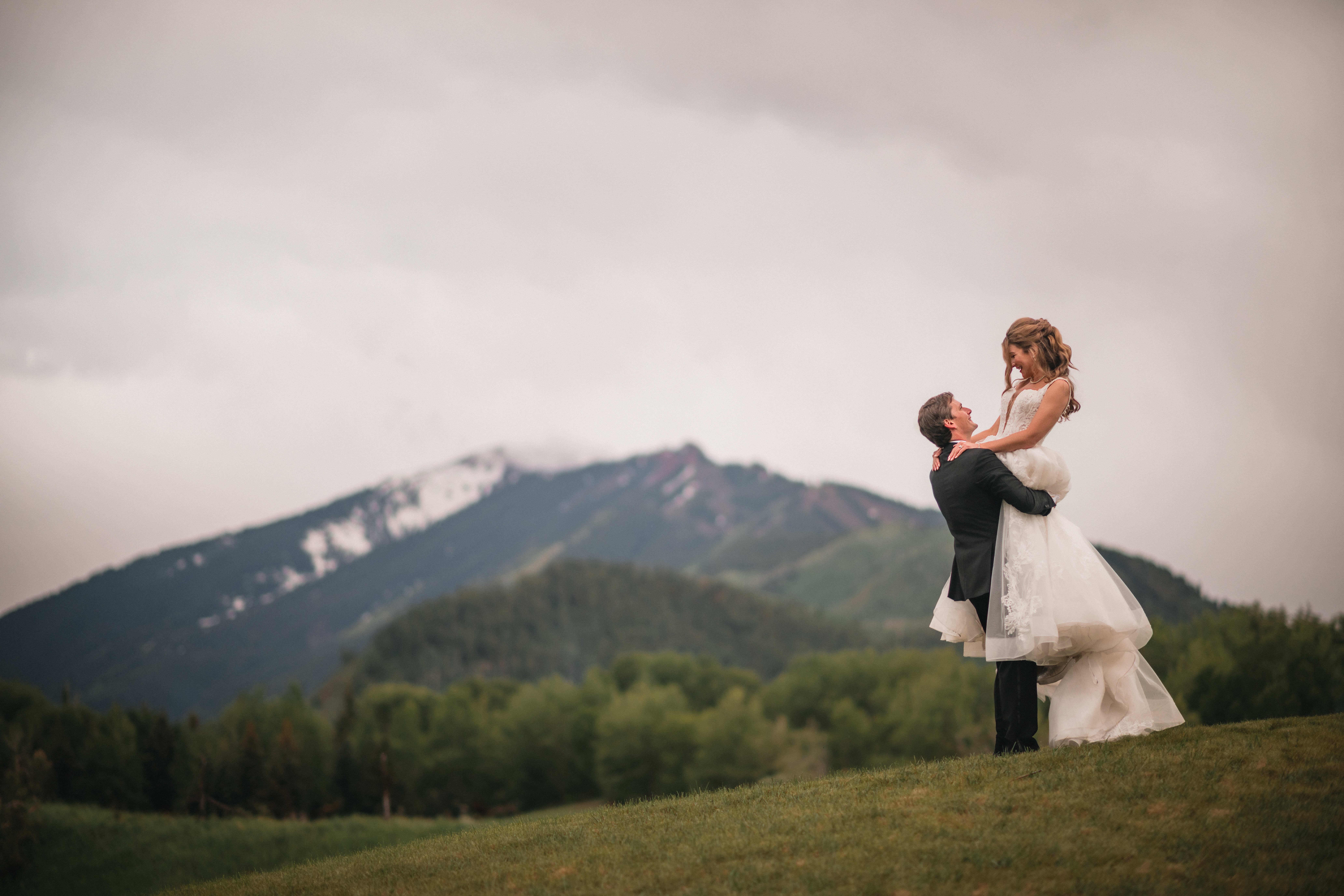 Bride and groom looking at each other as the groom lifts her in front of the scenic mountain view.
