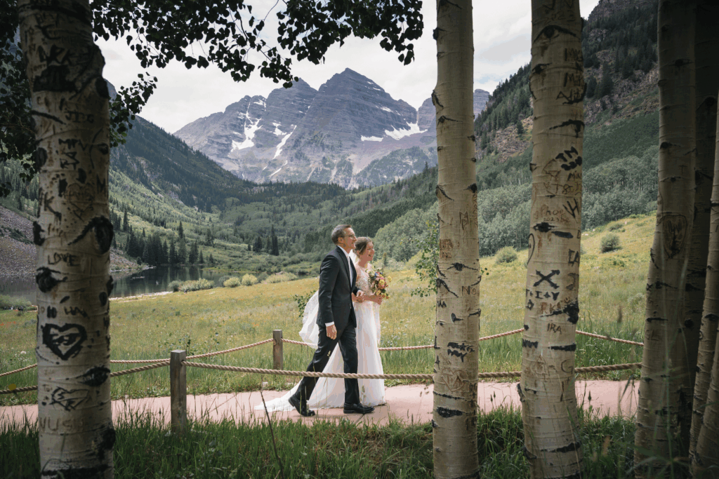 Father walking his daughter down a mountain path toward a wedding ceremony at Maroon Bells.