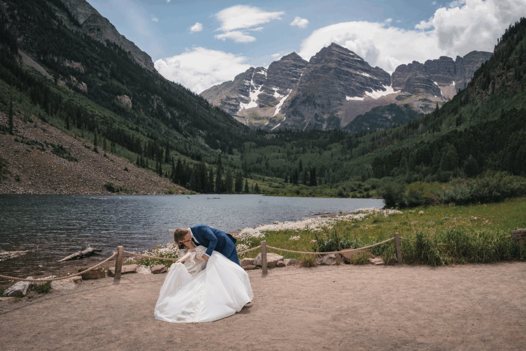 Groom dips his wife and kisses her in front of the lake at Maroon Bells.