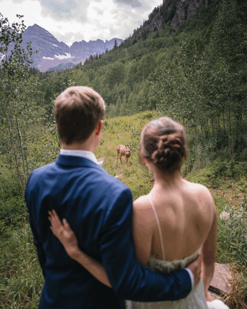 New husband and wife stand with arms around each other as they watch a deer in Maroon Bells.