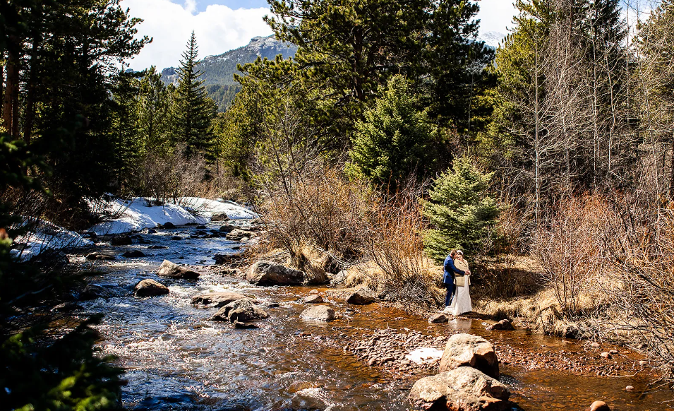 Bride and groom standing beside the flowing river at Wild Basin Lodge after their wedding.