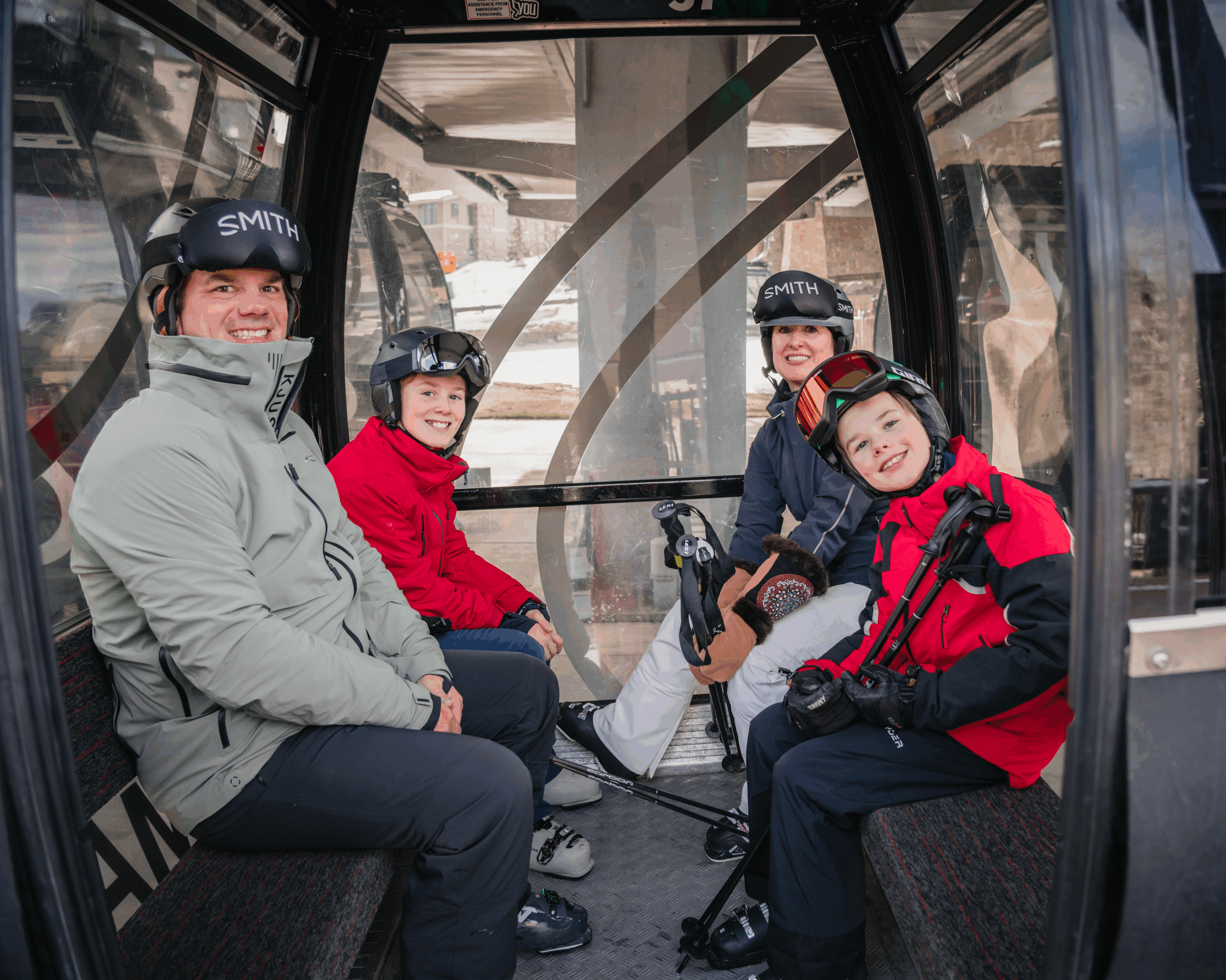 A family of four sits inside a ski gondola, smiling for an Aspen ski trip photographer before heading up the snow-covered mountain.