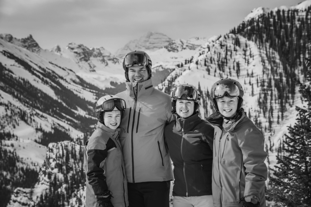 Black and white photo of a family of four posing on the slopes of the snowy mountains in Colorado.