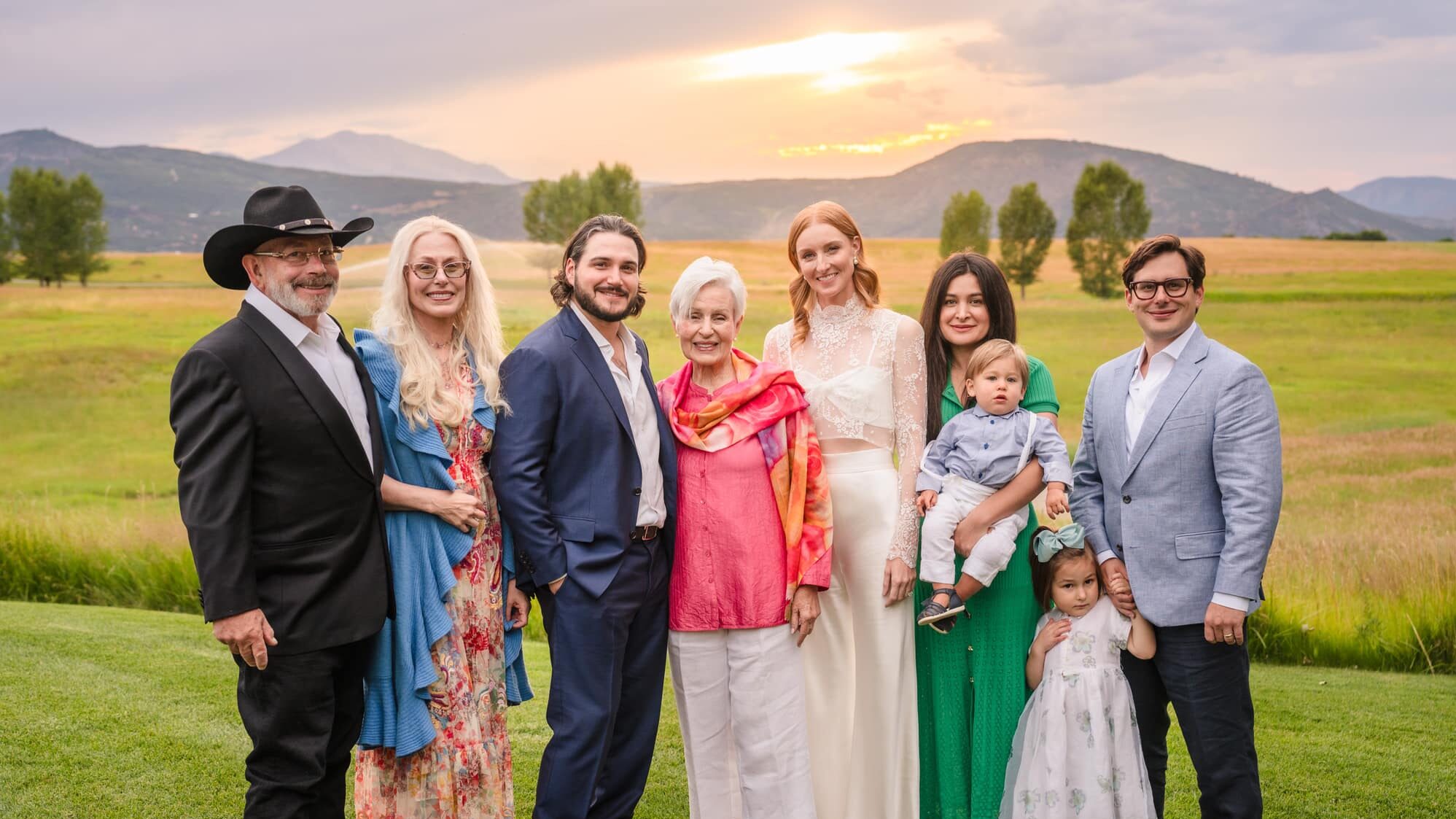 Outdoor wedding family portrait with multiple generations gathered in a scenic mountain field at sunset, a warm and natural Photo Booth Alternative highlighting genuine connection and setting.