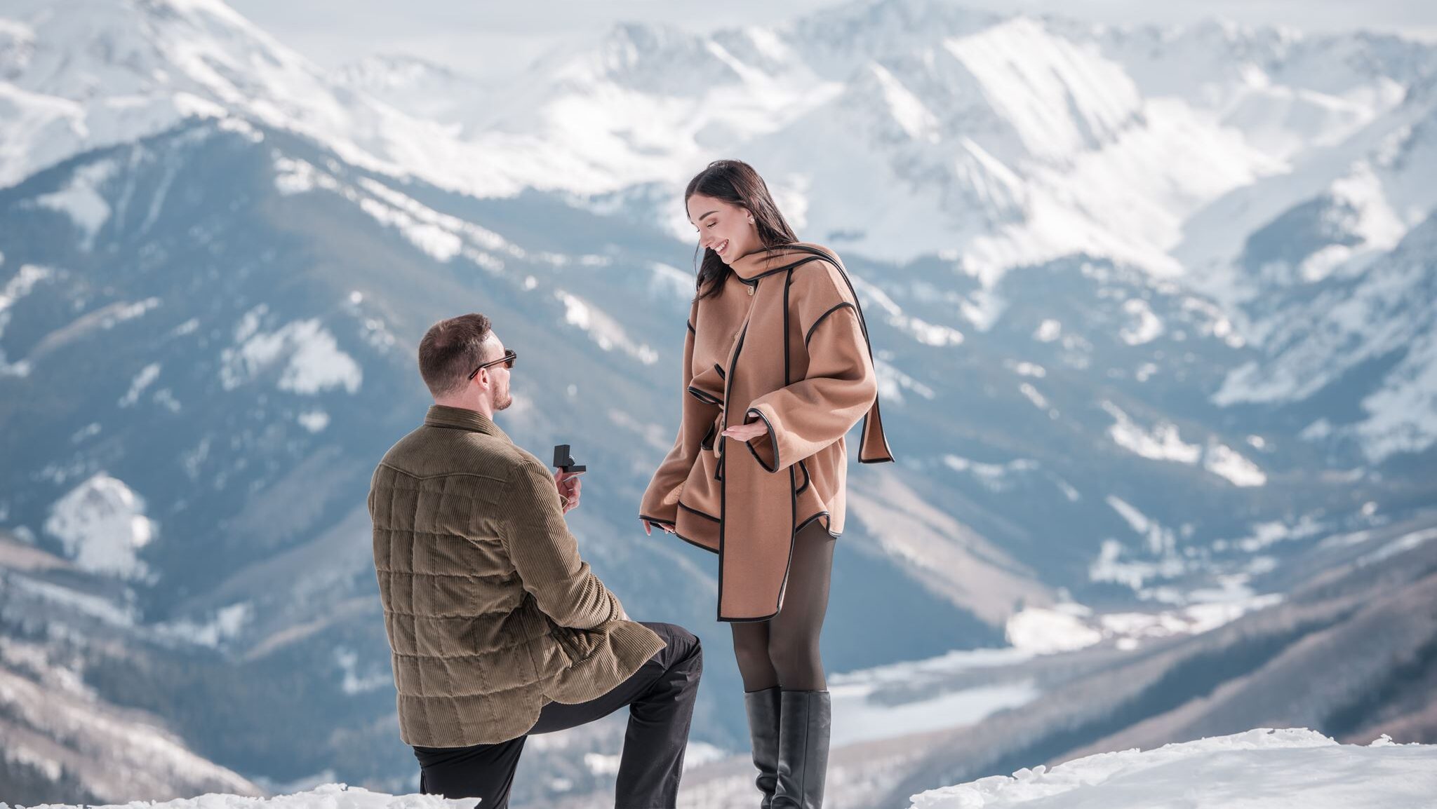 Aspen proposal photographer capturing the moment a groom proposes on one knee in the snow, Elk Mountains spanning behind them