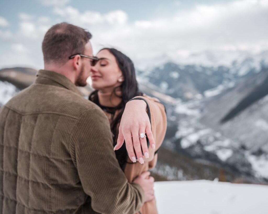 Where to propose in Aspen Colorado couple kissing after surprise proposal with snow covered mountain ridgeline in background