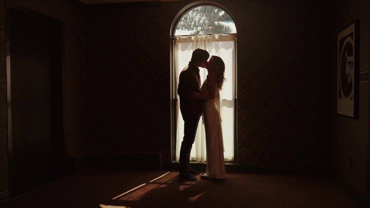 Couple silhouette kissing inside Hotel Jerome Aspen backlit by arched window with mountain view